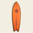 An orange Almond Surfboards surfboard with brown edges and a swallowtail design stands vertically against a light background. The board features a black logo of two palm trees and a person near the top, plus blue text near the bottom.