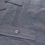 Close-up of a gray technical cotton-poly stretch fabric, showing two embroidered chevron insignias above a pocket with a button. The stitching, texture, and unique embroidery details are clearly visible.