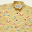 A yellow Mansfield Shirt with unique seasonal patterns of pink flamingos, palm trees, and small islands. This lightweight cotton-poly shirt features a front pocket and a Howler label inside the collar.