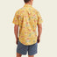 A man wearing the Mansfield Shirt—a lightweight cotton-poly shirt with unique seasonal patterns featuring tropical flamingos—and blue shorts stands facing away from the camera against a light background.