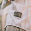A close-up of a vintage inspired Howler Brothers pearl snap shirt, white with blue stripes and a patch reading Land Cruiser Howler Brothers with a simple car graphic, worn outdoors.