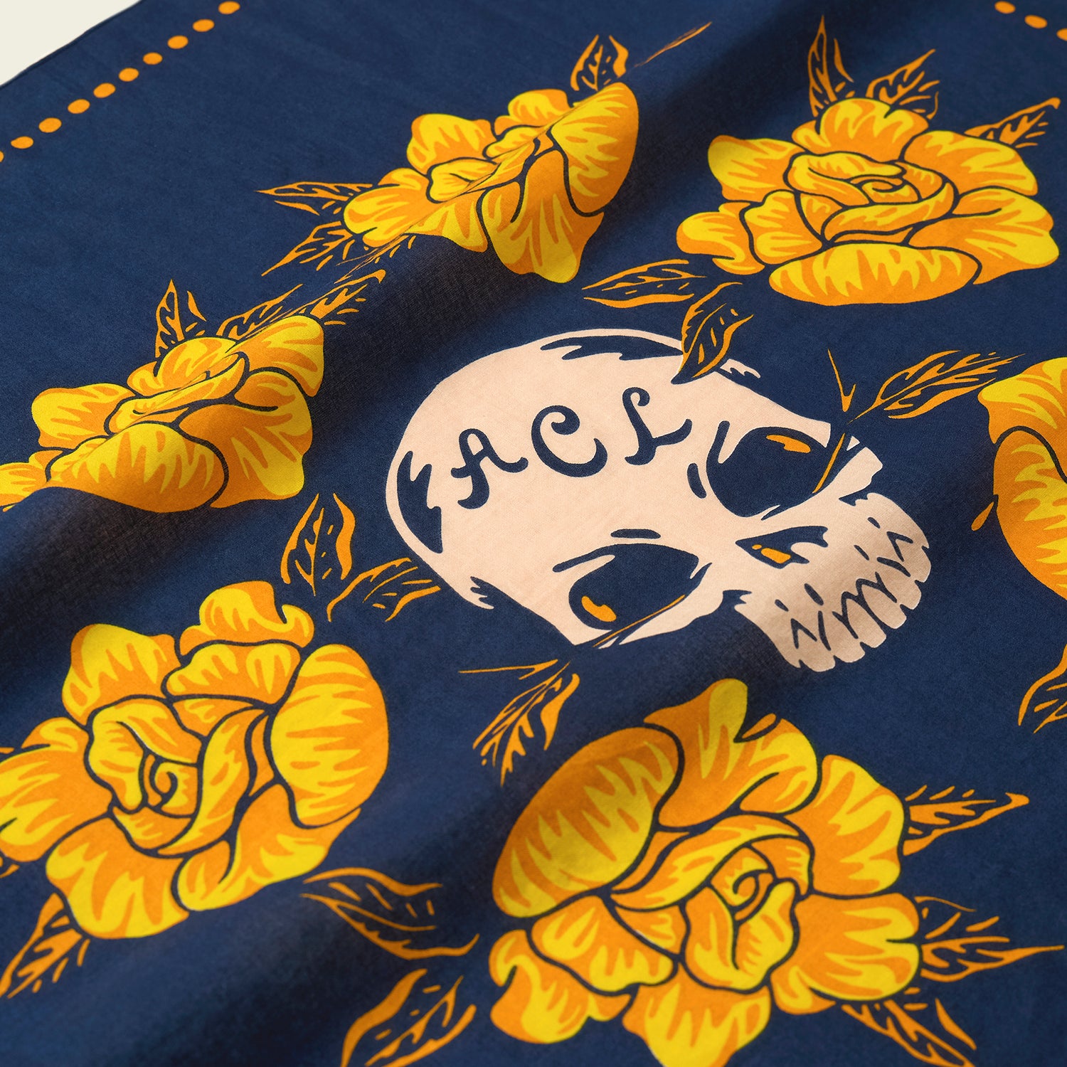 A blue fabric from the Yellow Rose Collection features bright yellow roses and a white skull with ACL written on its forehead, surrounded by leaves and orange dotted accents along the edge—perfect for Howler Bandanas at the ACL Festival. - View 5