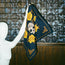 A white mannequin holds up a navy blue scarf from the Yellow Rose Collection, decorated with yellow flowers and a skull with RIP on its forehead. The background features patterned wallpaper and a wooden panel.