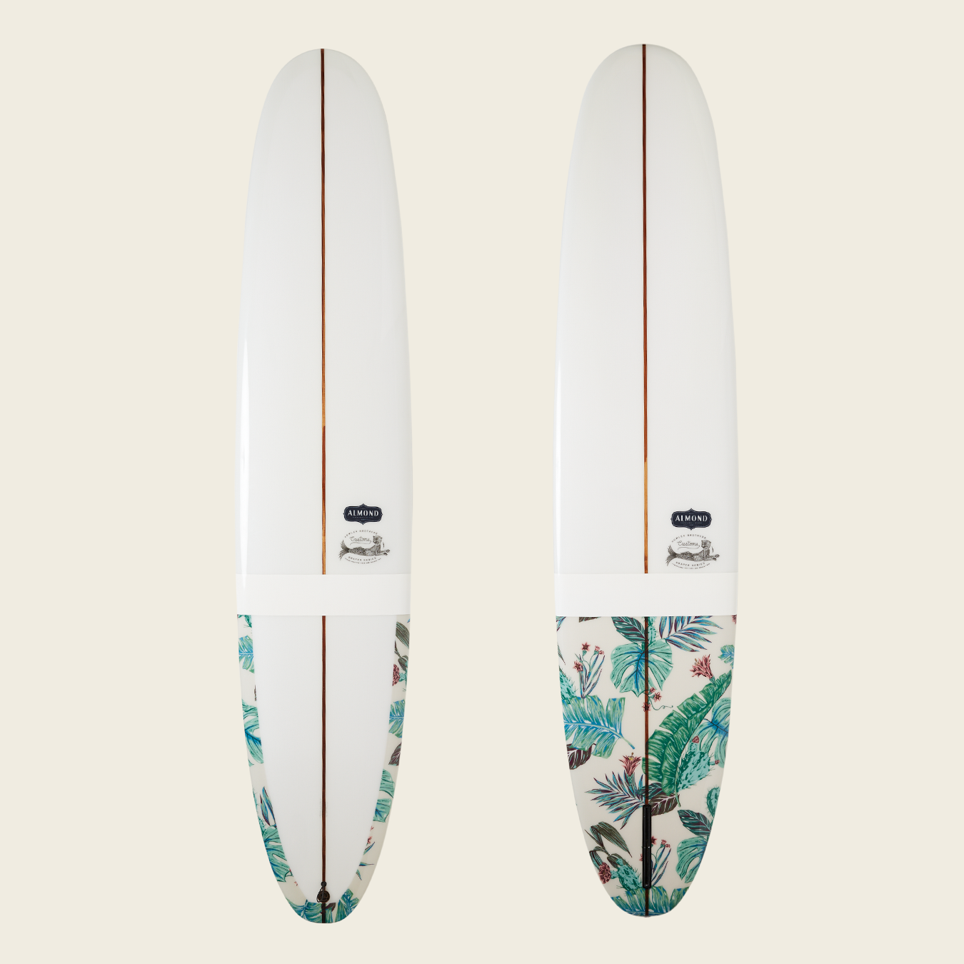 Two white longboards are shown upright against a light background. The lower third of each board features a tropical leaf pattern in green and blue tones, while a brown stripe runs down the center, highlighting their versatile handling. - View 1