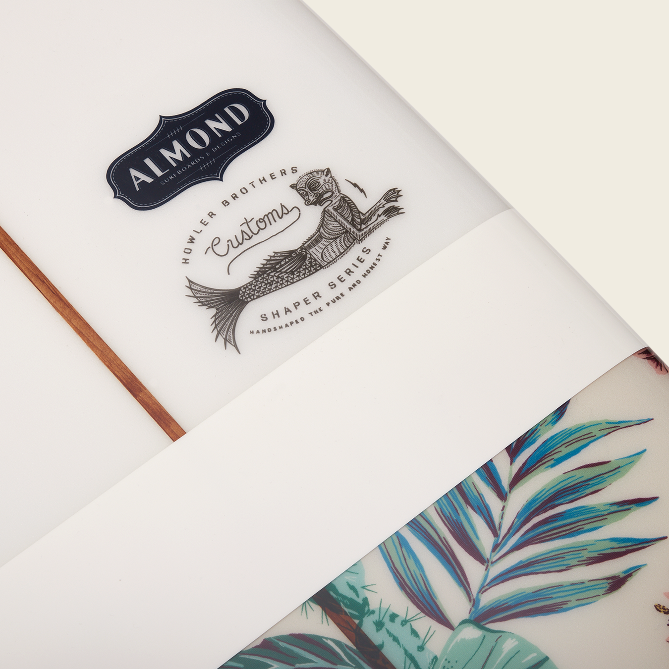 Close-up of a Surf Thump longboard featuring the Almond brand logo, a mermaid illustration labeled “Hokler Brothers Customs Shaper Series,” and part of a tropical leaf design, highlighting its versatile handling. - View 2
