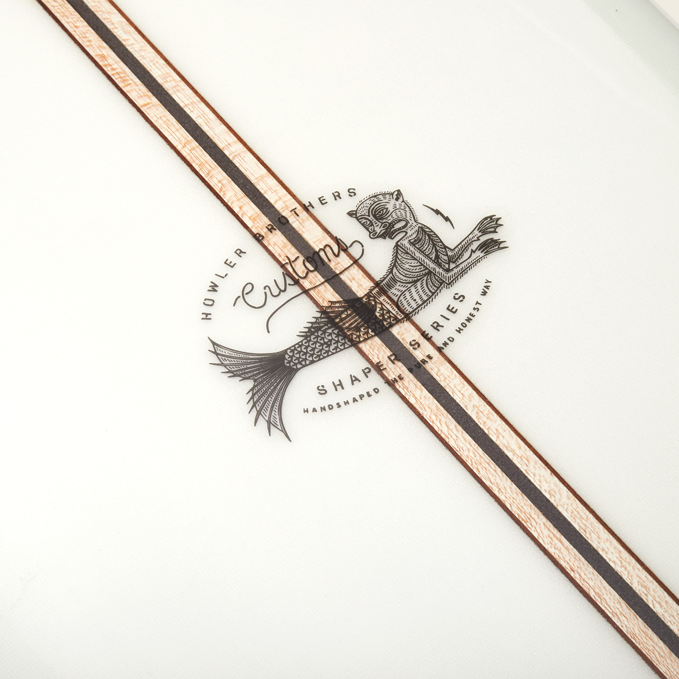 Close-up of a traditional surfboard featuring a logo with a fish and the words “Howler Brothers Custom Shapes Series,” plus two parallel wood inlays running diagonally across the white surface, reminiscent of classic noseriding boards. - View 2