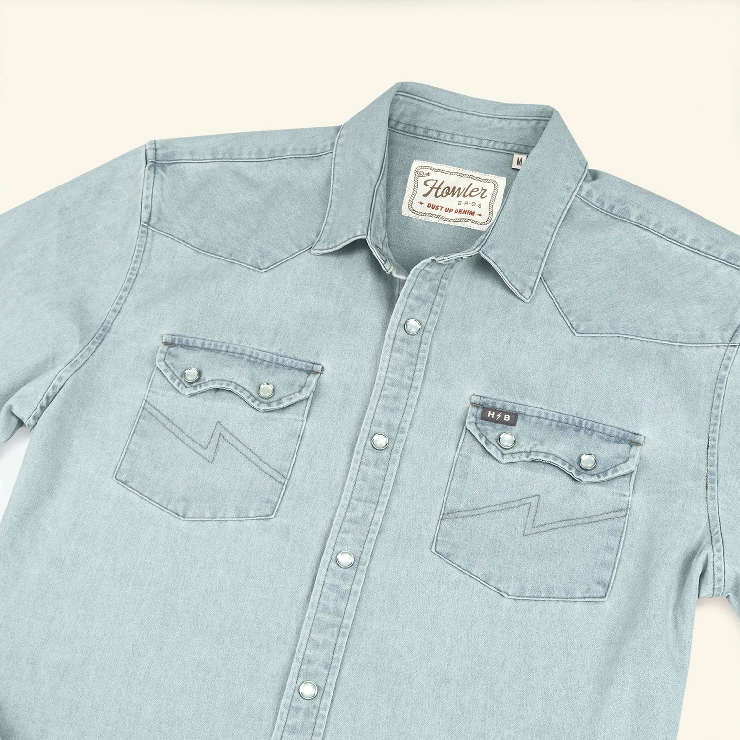 A light blue Denim Snapshirt with rugged denim construction, two chest pockets featuring pointed flaps and zigzag stitching, silver snap buttons, and a Howler brand label on the inside collar—perfect for versatile style. - View 5