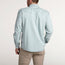 A man stands facing away, wearing a light blue Denim Snapshirt and beige pants against a plain, light background—showcasing a versatile style perfect for any occasion.