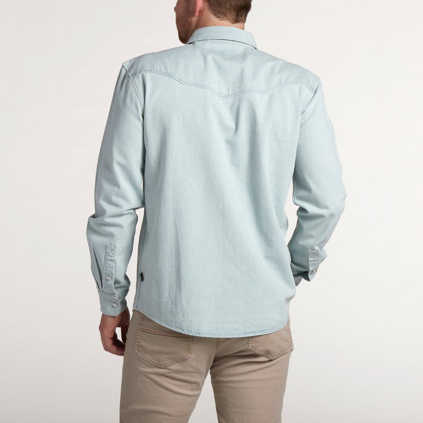 A man stands facing away, wearing a light blue Denim Snapshirt and beige pants against a plain, light background—showcasing a versatile style perfect for any occasion. - View 4