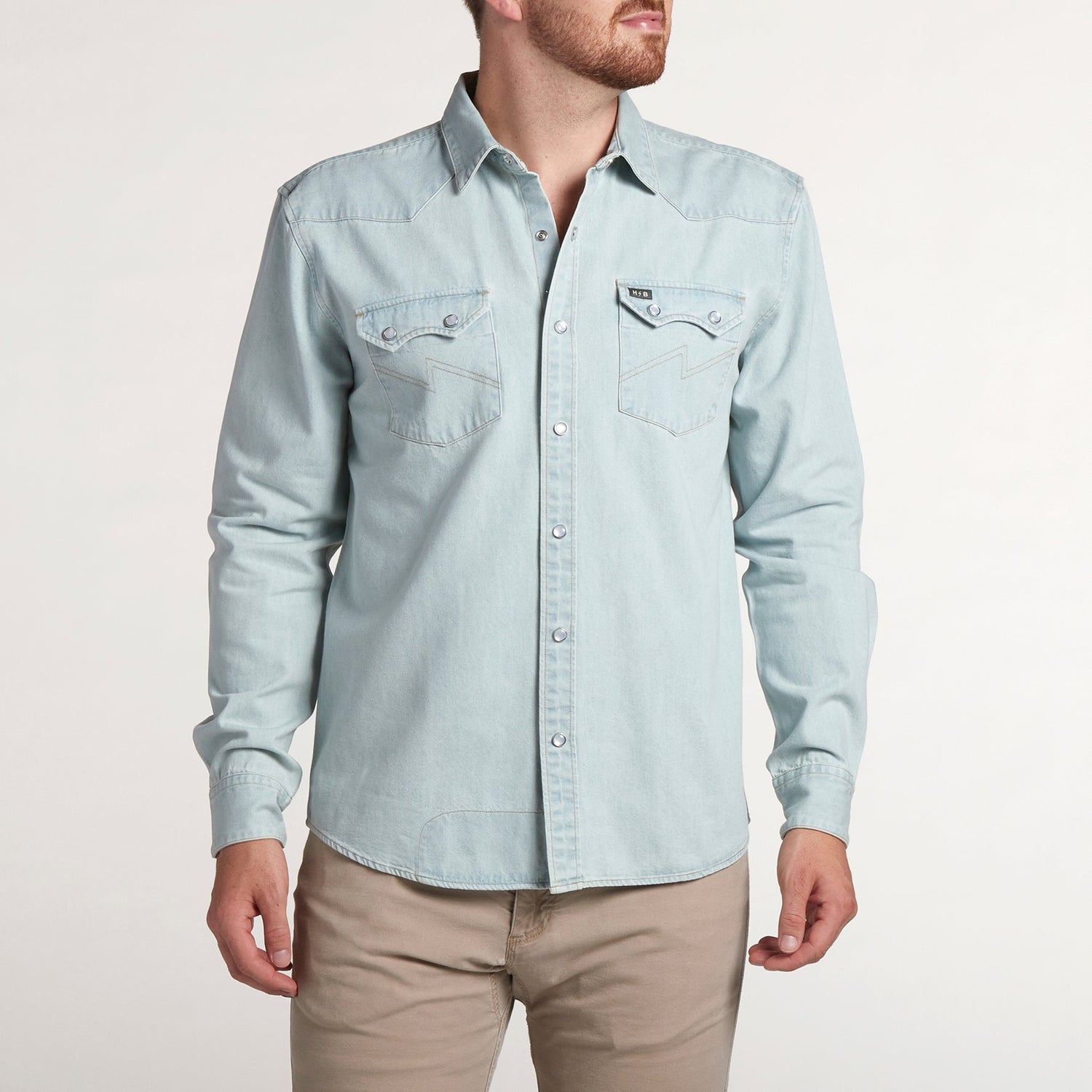 A man wearing a rugged denim shirt with two chest pockets and beige pants stands against a plain, light-colored background, showcasing a versatile style as he turns his head slightly to the side. - View 3