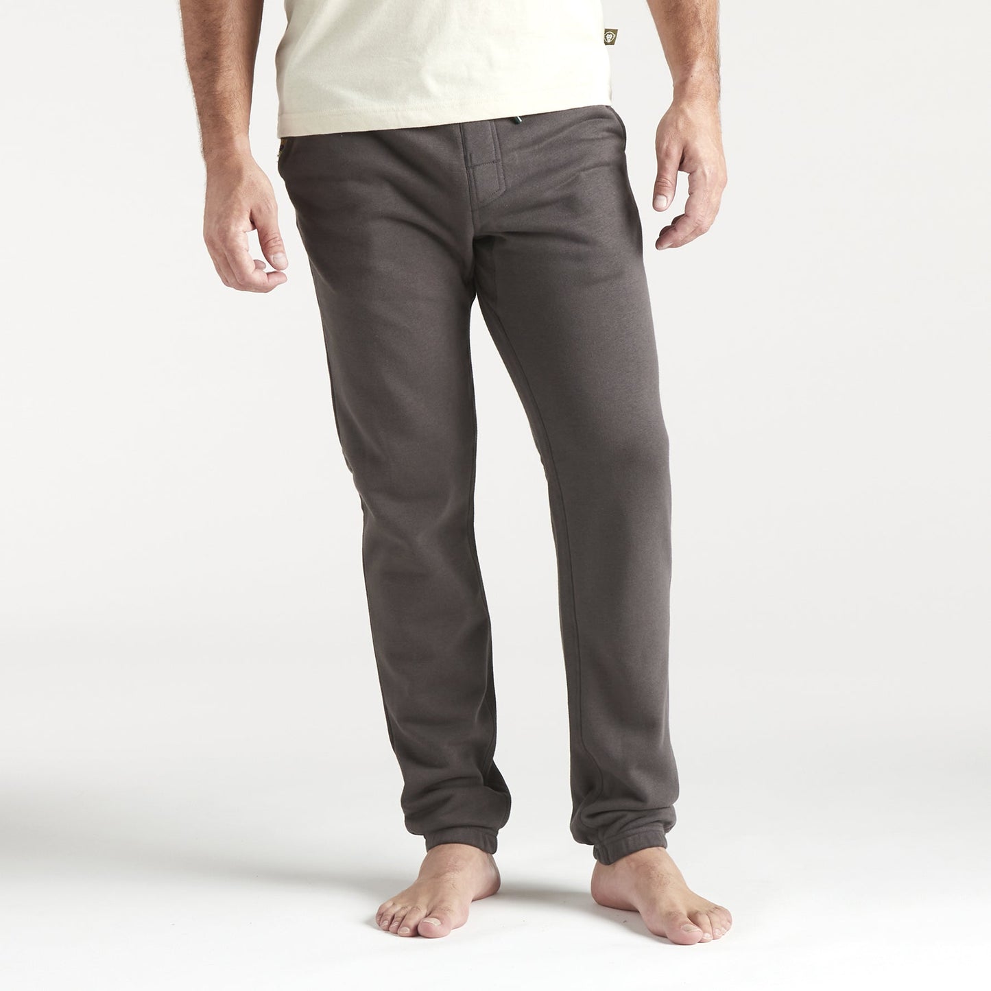 A person stands barefoot, wearing fitted dark gray French terry sweatpants with a drawstring waistband and a light-colored shirt, arms relaxed by their sides against a plain white background. The photo is cropped at the shoulders. - View 2