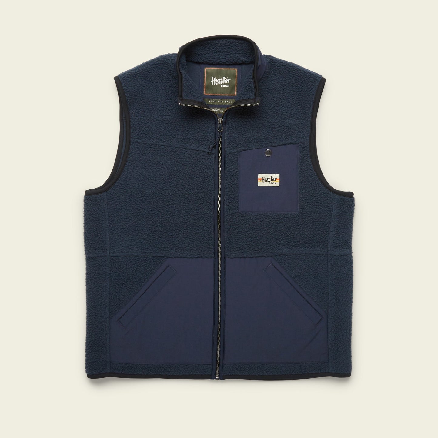 A navy blue Chisos Fleece Vest with a front zipper, two lower front pockets, and a chest pocket featuring a rectangular “Howler Brothers” logo patch. This lightweight vest has a high collar and contrasting high pile fleece fabric panels. - View 6