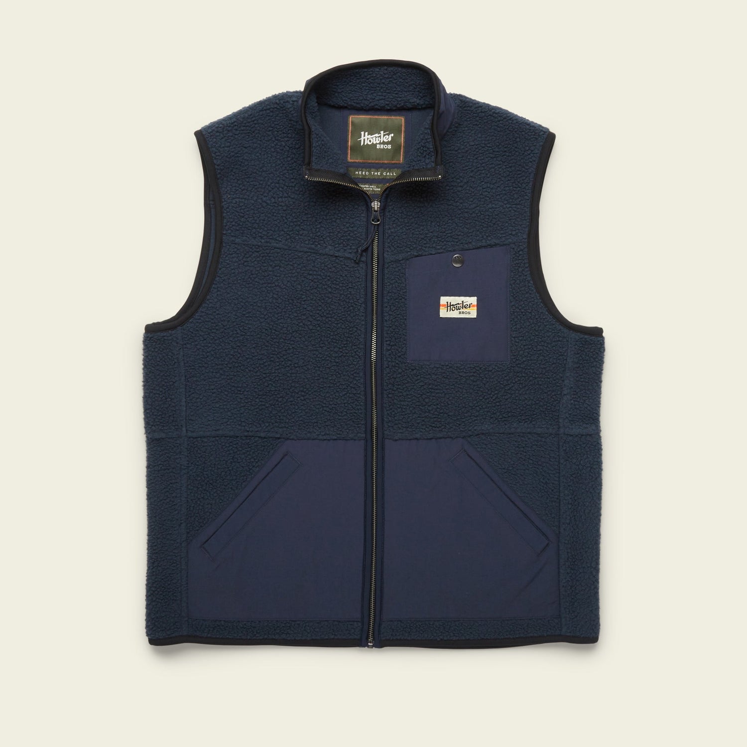 A navy blue Chisos Fleece Vest with a front zipper, two lower front pockets, and a chest pocket featuring a rectangular “Howler Brothers” logo patch. This lightweight vest has a high collar and contrasting high pile fleece fabric panels. - View 6