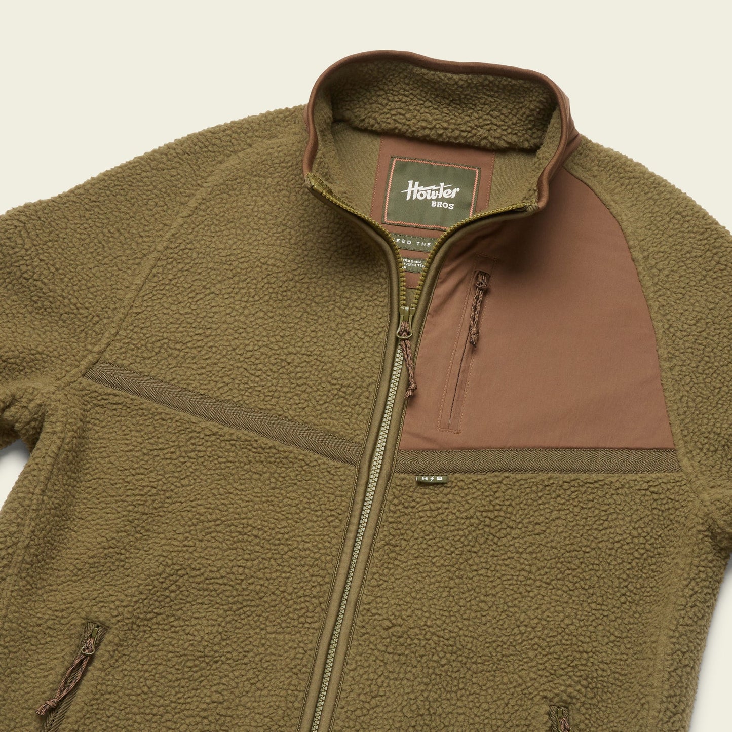 A brown polyester fleece jacket with a front zipper, high collar, and a chest pocket featuring a contrasting panel. The soft and fluffy texture adds comfort, while the label inside reads Howler Bros Howler Crozet. - View 6