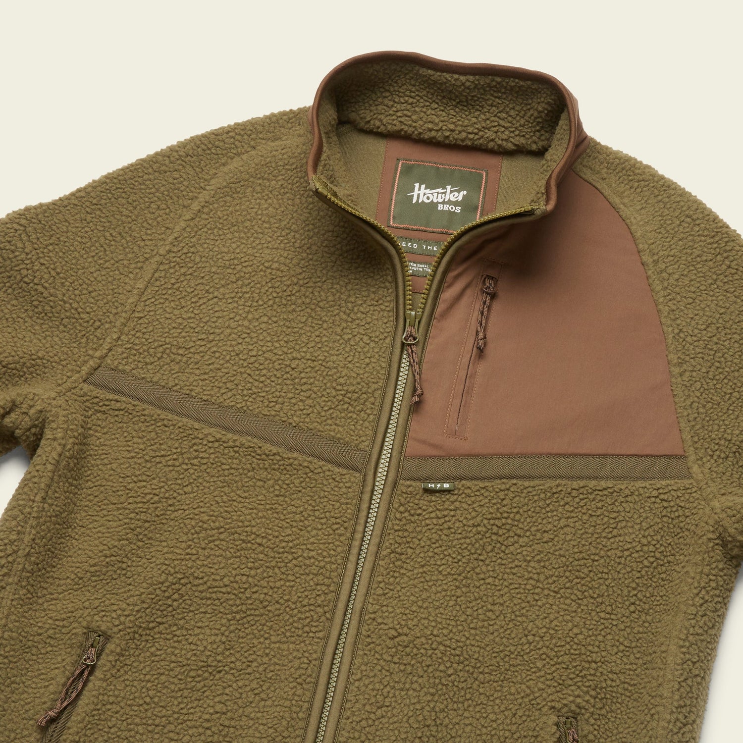 A brown polyester fleece jacket with a front zipper, high collar, and a chest pocket featuring a contrasting panel. The soft and fluffy texture adds comfort, while the label inside reads Howler Bros Howler Crozet. - View 6