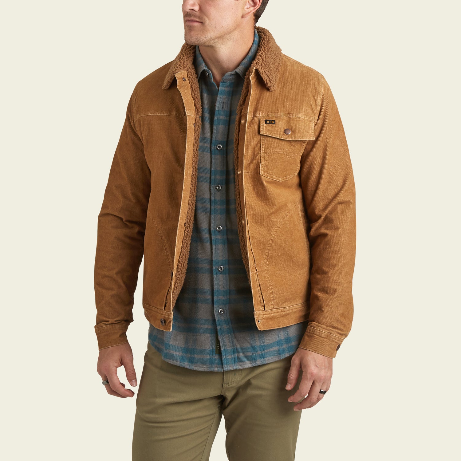 A man wearing a brown Fuzzy Depot Jacket with a sherpa lining over a blue plaid shirt and khaki pants stands facing slightly to the left, with his left hand in his pocket. - View 4