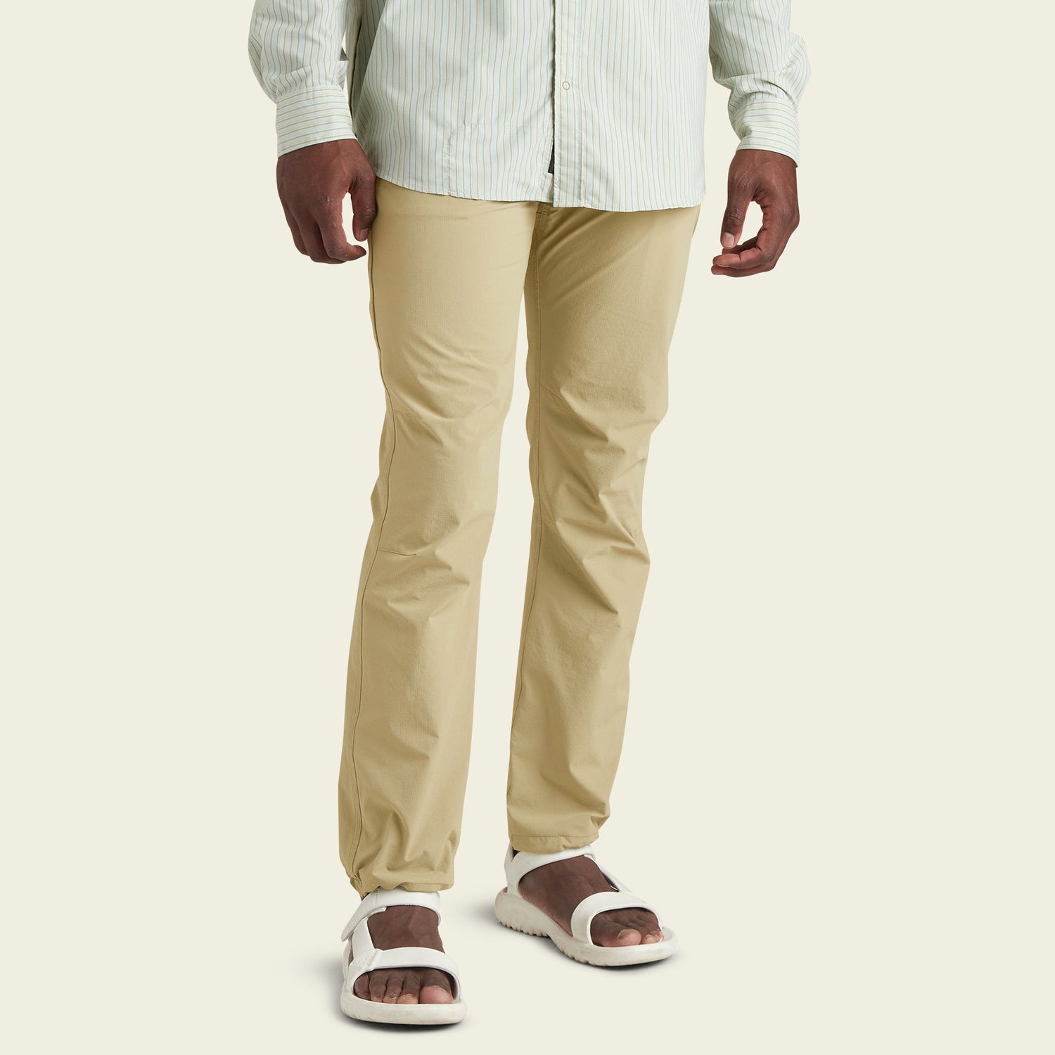 A person wearing light beige stretch nylon pants, a light green and white striped shirt, and white sandals stands against a plain, light background. The image shows the person from mid-chest down. - View 3