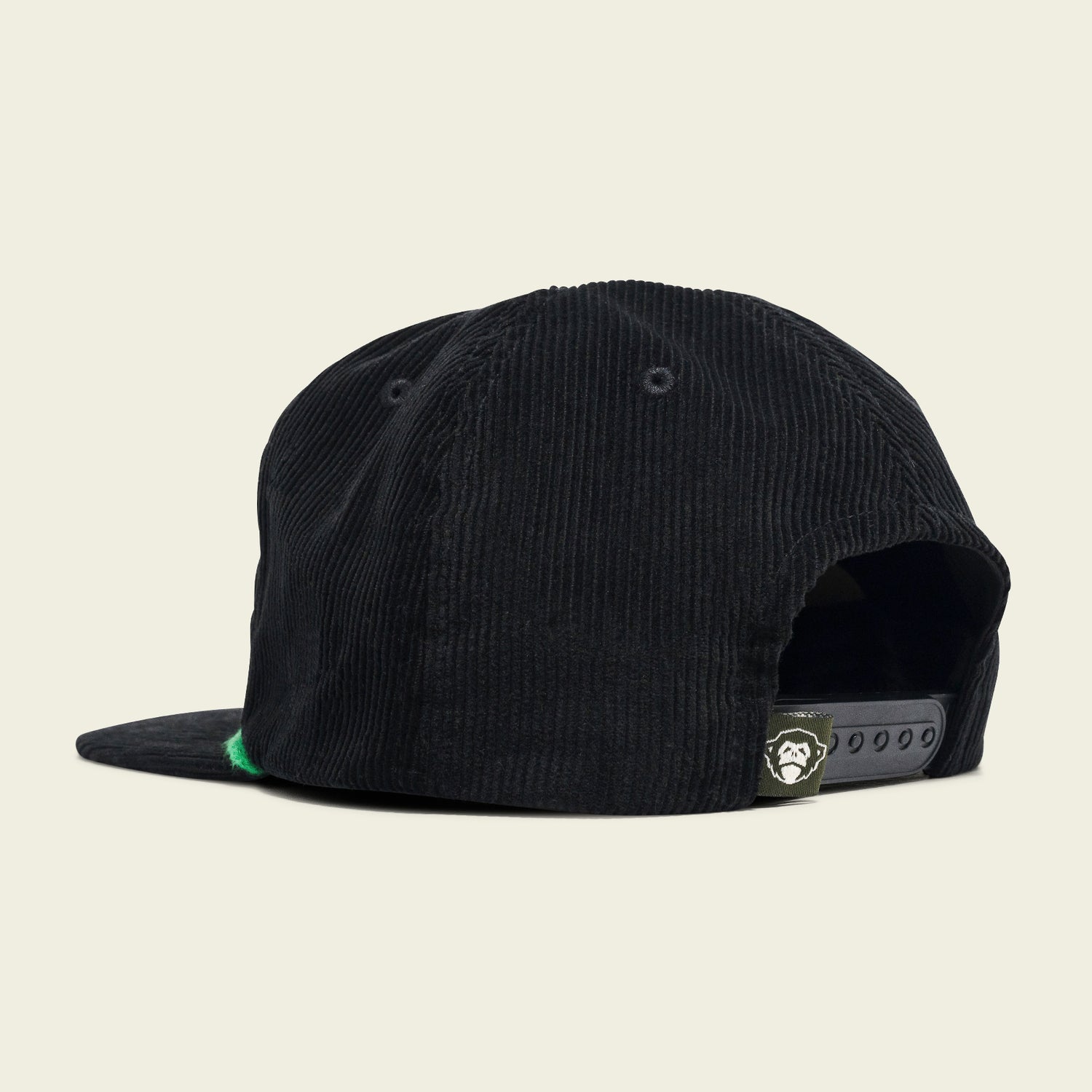 A black corduroy Unstructured Snapback from the 2024 Verde Collection, shown from the back-left side, features an adjustable strap and a small label with a white cartoon gorilla face above the opening. - View 3