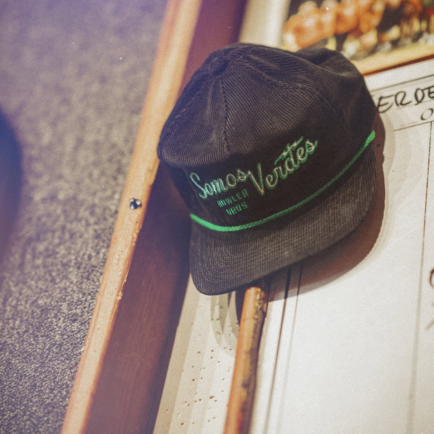 A black Unstructured Snapback corduroy cap with green embroidery reading Somos Verdes from the 2024 Verde Collection rests on a pinball machine, with a pool cue nearby—showcasing Austin FC spirit. - View 5