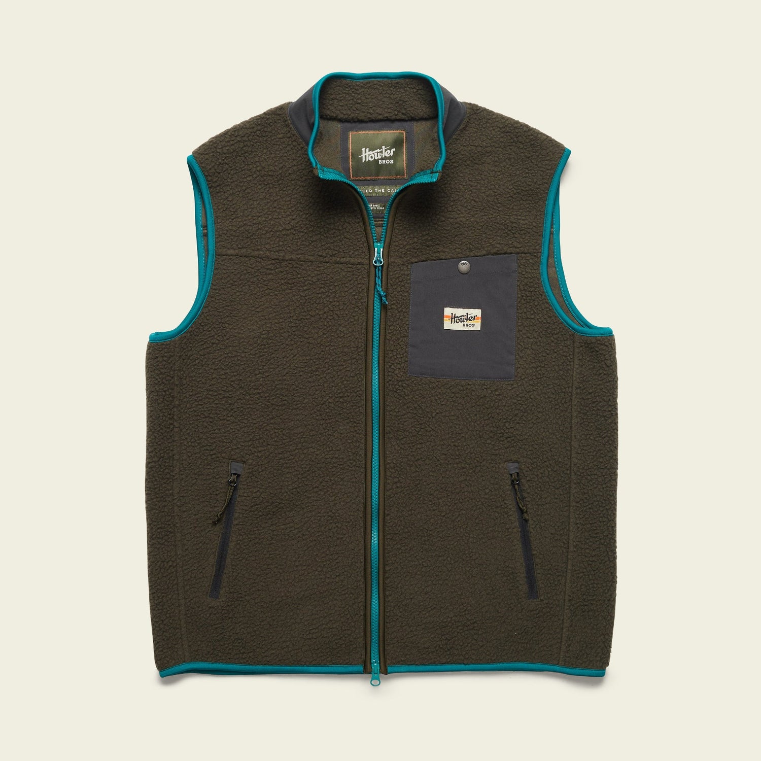 A dark green Chisos Fleece Vest with teal trim, made from high pile fleece. This lightweight vest features a front zipper, two zippered hand pockets, and a black chest pocket with a button and rectangular Howler Bros logo patch.