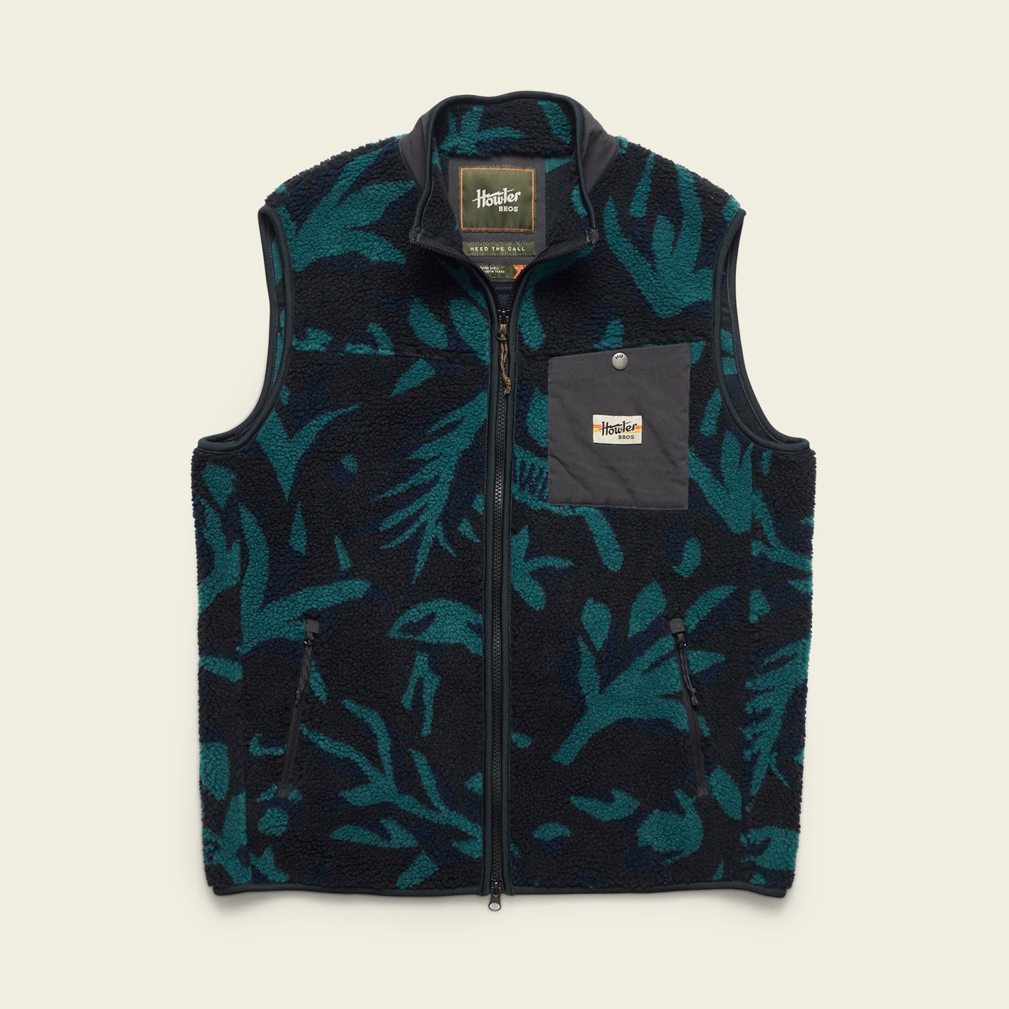 The Chisos Fleece Vest is a lightweight vest featuring a dark blue and teal leafy pattern, high pile fleece, a full front zipper, high collar, and a gray chest pocket with a rectangular “Howler Bros” logo patch. - View 1