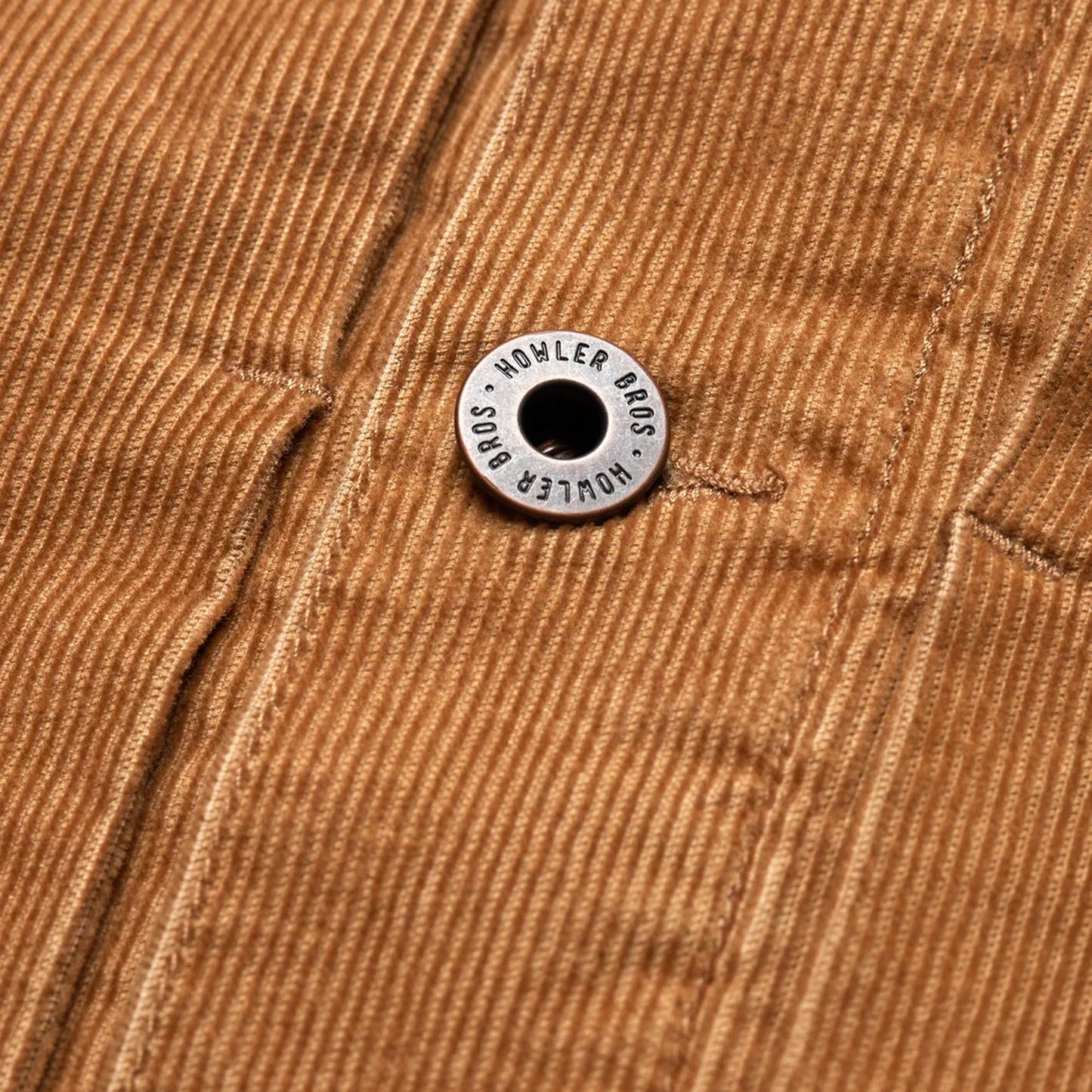 Close-up of a brown corduroy jacket from the Fuzzy Depot Jacket collection, featuring a metal button engraved with HOWLER BROS attached to a seam running vertically through the fabric. - View 7