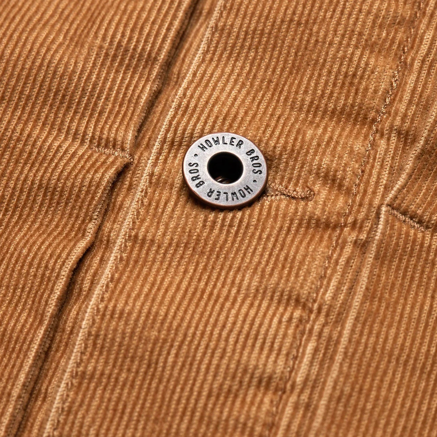 Close-up of a brown corduroy jacket from the Fuzzy Depot Jacket collection, featuring a metal button engraved with HOWLER BROS attached to a seam running vertically through the fabric. - View 7
