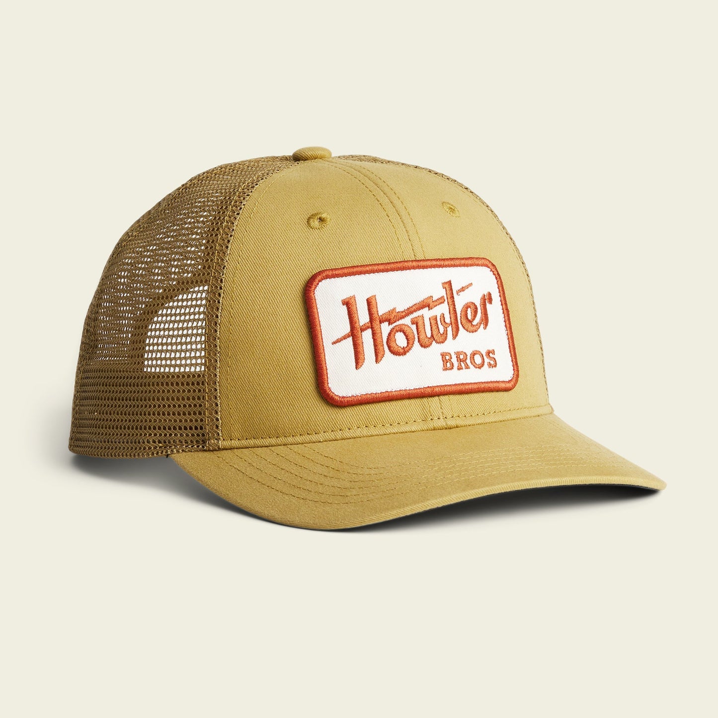 A tan mesh trucker hat with a curved brim and a rectangular patch on the front reading Howler Bros in red and orange letters. This adjustable hat features classic Howler artwork and is displayed on a plain light background. - View 9