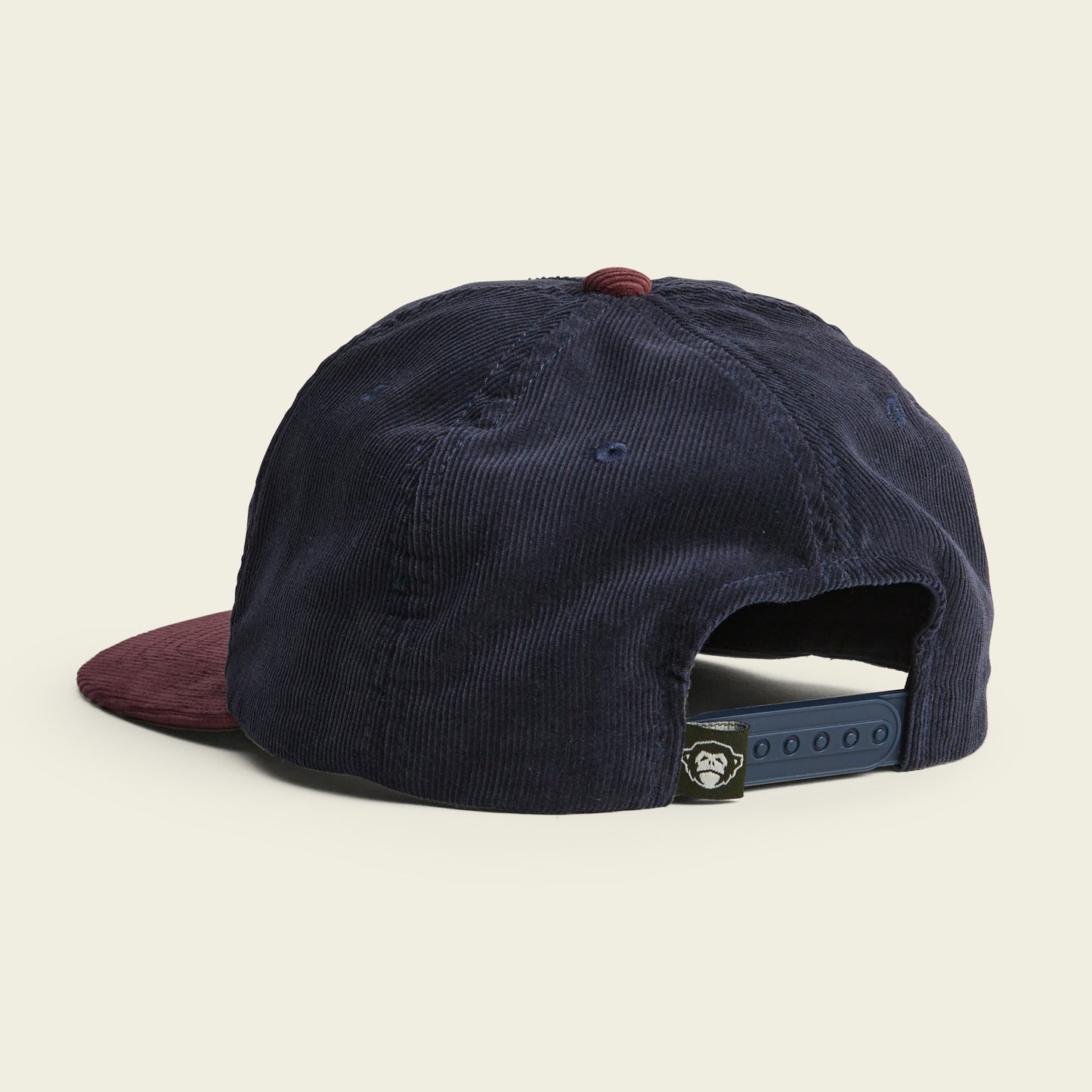 A corduroy Unstructured Snapback cap viewed from the back, featuring a navy blue soft crown, maroon button on top, and maroon brim. The black adjustable snapback closure includes a small logo tag attached. - View 3