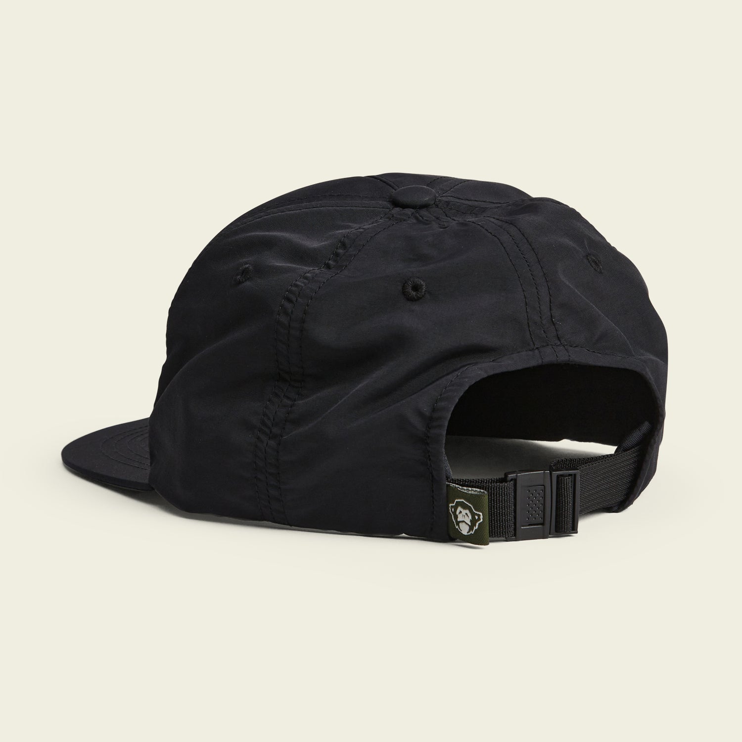A black baseball cap shown from the back, featuring an adjustable strapback closure with a buckle and a small tag displaying a stylized face logo. The unstructured strapback design offers a soft crown. The background is a plain off-white color. - View 3