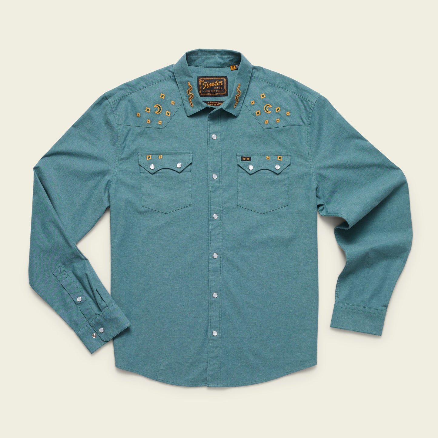 A teal long-sleeve western shirt in stretch chambray, featuring pearl snaps, two chest pockets, and gold vintage inspired motif embroidery of stars and cacti on the yoke. The shirt is laid flat on a light background. - View 10