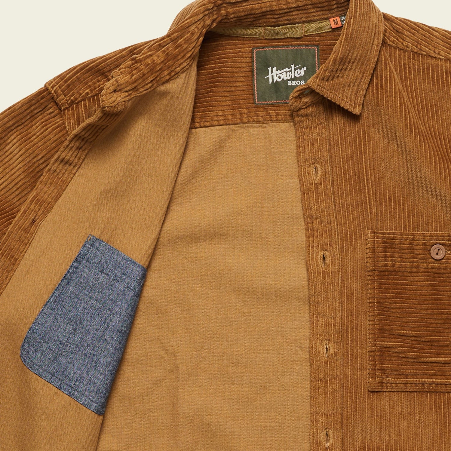 A brown wide wale corduroy travel shirt with the front open, revealing a blue inner pocket. The Iquitos Overshirt features a chest pocket and a Howler Bros label sewn inside the collar. - View 6