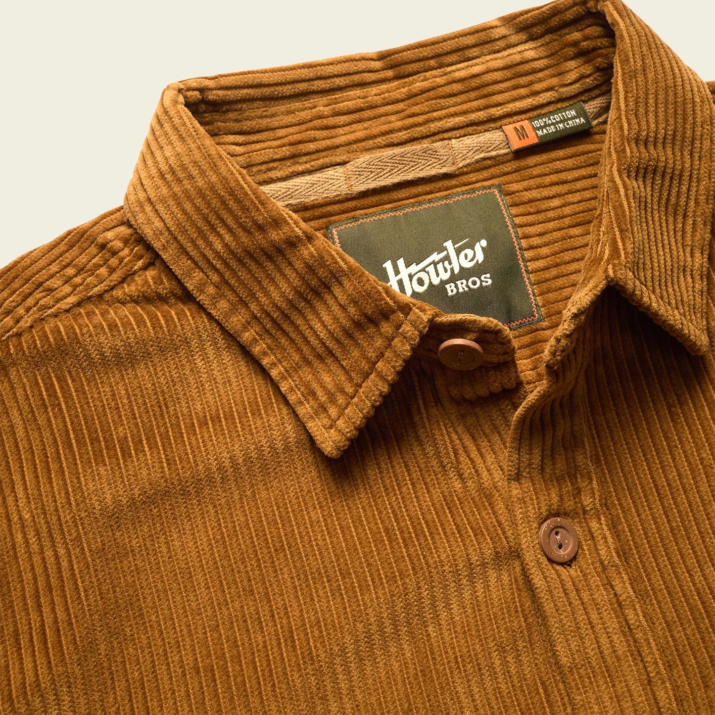 A brown wide wale corduroy button-up shirt with a collar, featuring two labels inside the neck area: one says Howler Bros, and the other indicates it is a medium size and made in Vietnam. - View 7