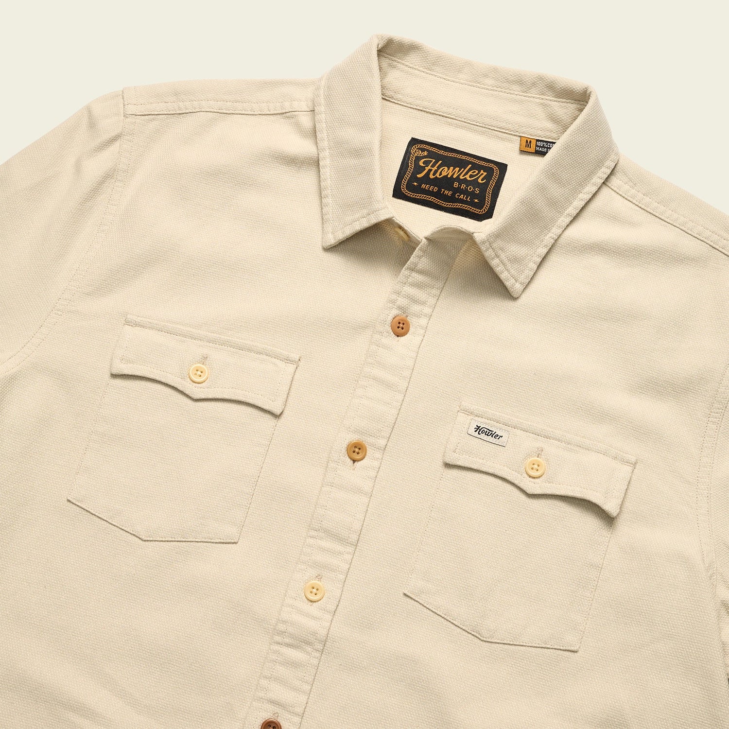 A beige western shirt with a collar, two front chest pockets with button flaps, and brown buttons. The Novato Shirt features a visible Howler Bros brand tag inside the collar and above the left pocket. - View 7
