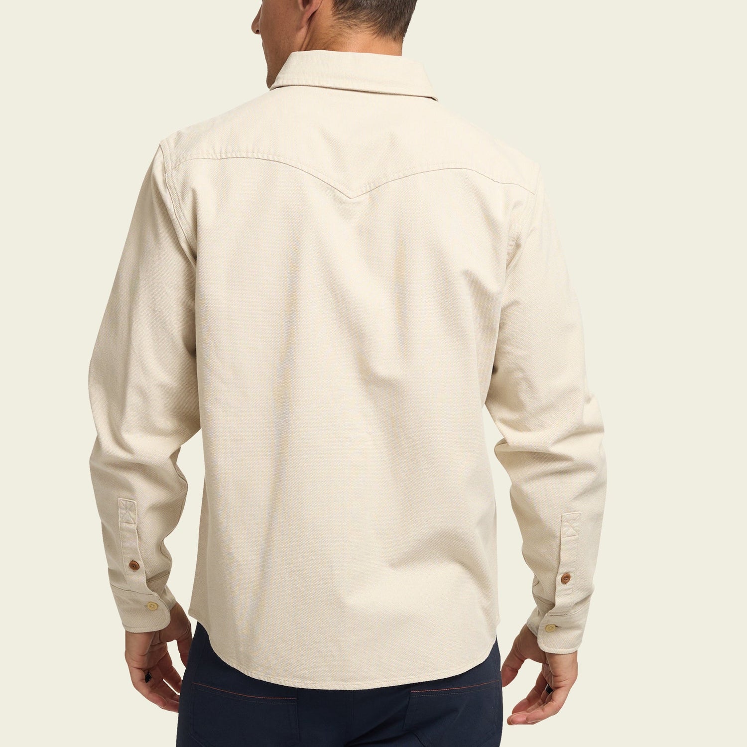 A man wearing a cream-colored, long-sleeve Novato Shirt with a yoke detail on the back, shown from behind against a plain light background. - View 5