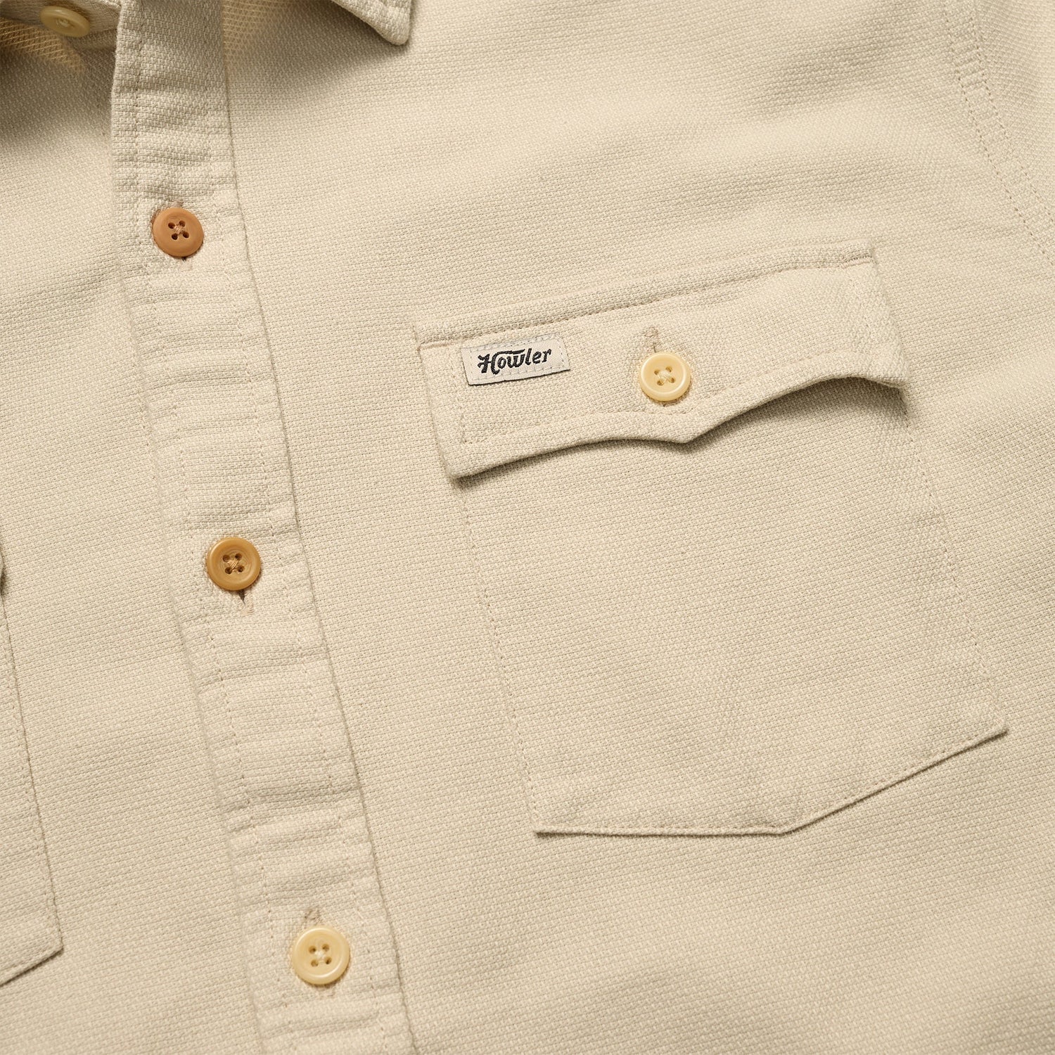 Close-up of a beige Novato Shirt, a classic western shirt with light brown buttons and a chest pocket. The pocket flap features a small Howler label and is secured by a button. - View 3