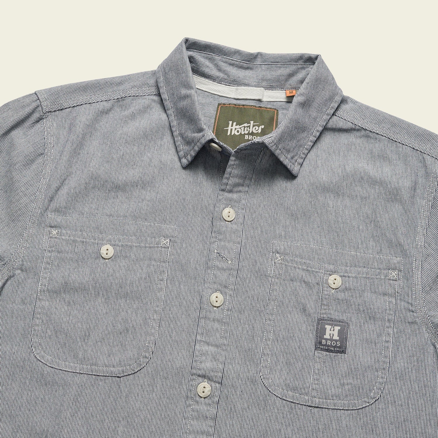 A blue and white striped cotton chambray Tallier Work Shirt with two front chest pockets—one featuring a H Bros patch—and a visible Howler Bros label inside the collar, inspired by classic American workwear. - View 6