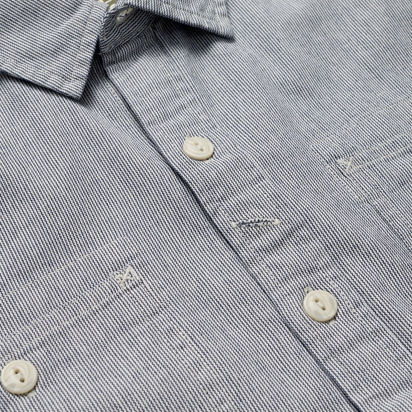 Close-up view of a light gray Tallier Work Shirt, crafted from cotton chambray, with white buttons and visible stitching details around the buttonholes and pockets—an elevated nod to classic American workwear. - View 3