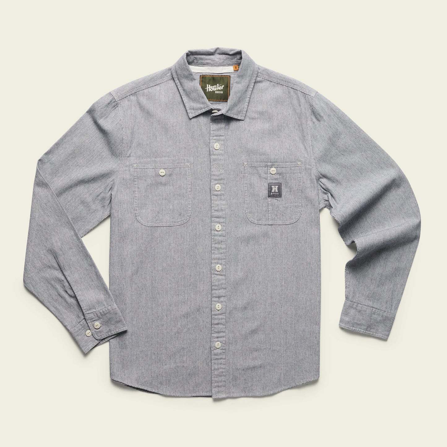 A long-sleeve, button-up light gray Tallier Work Shirt in cotton chambray with two chest pockets and white buttons, laid flat on a light background. A small rectangular tag is visible on the left pocket—classic American workwear style. - View 2