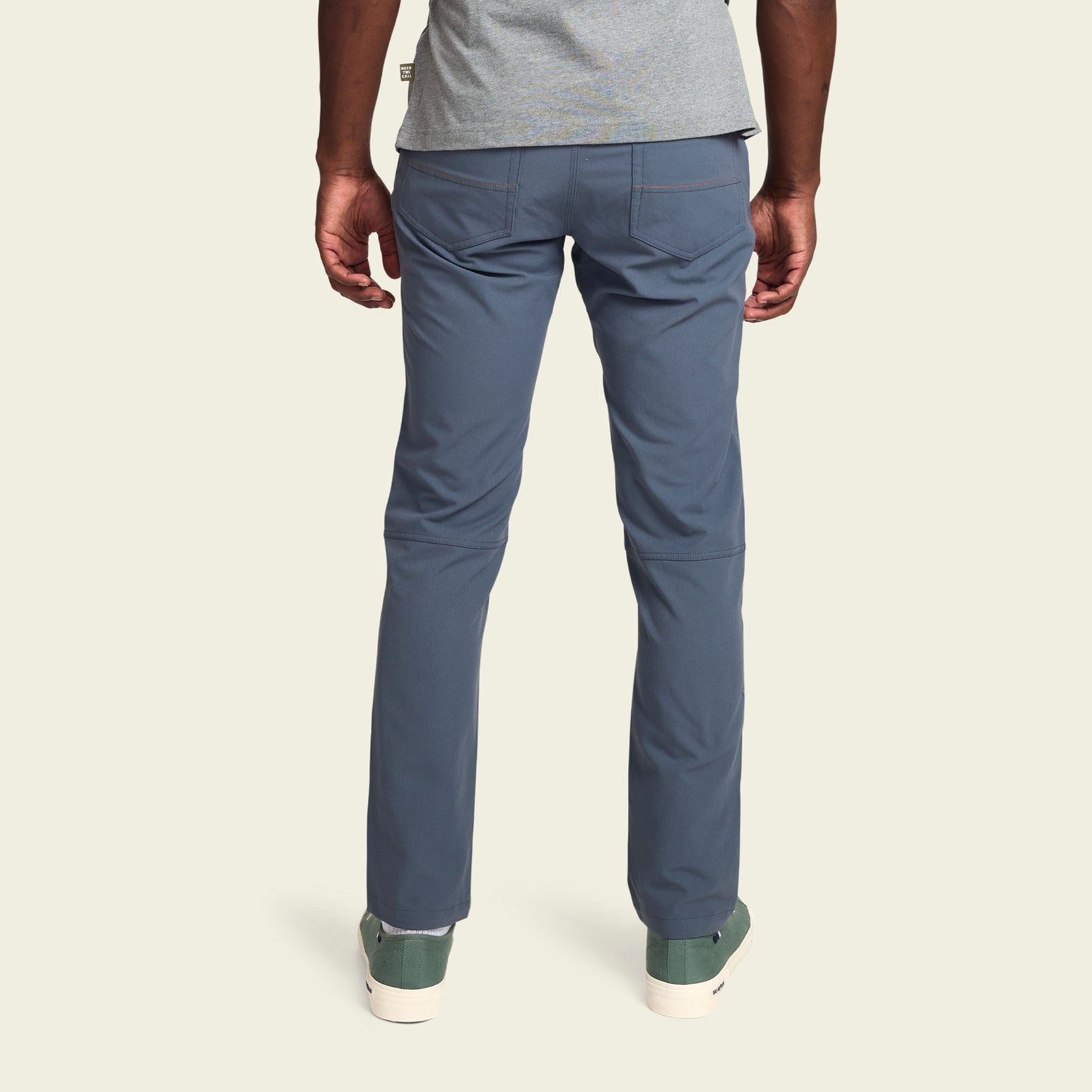 A person wearing blue tech fabric pants, a gray shirt, and green sneakers is standing with their back to the camera against a light, plain background. - View 5