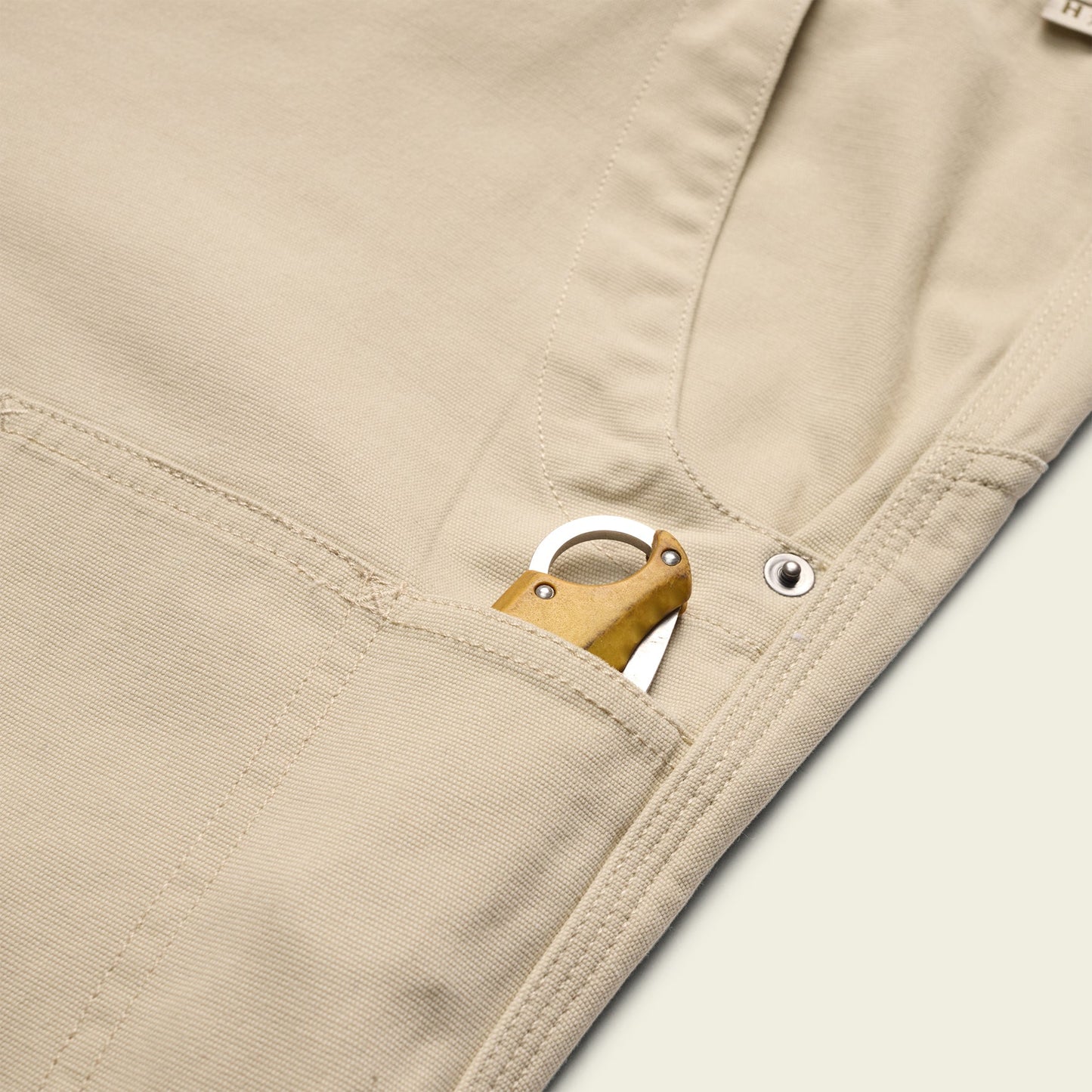 A close-up of rugged backcountry pants with a pocket knife featuring a brass handle partially visible in the front pocket. - View 5