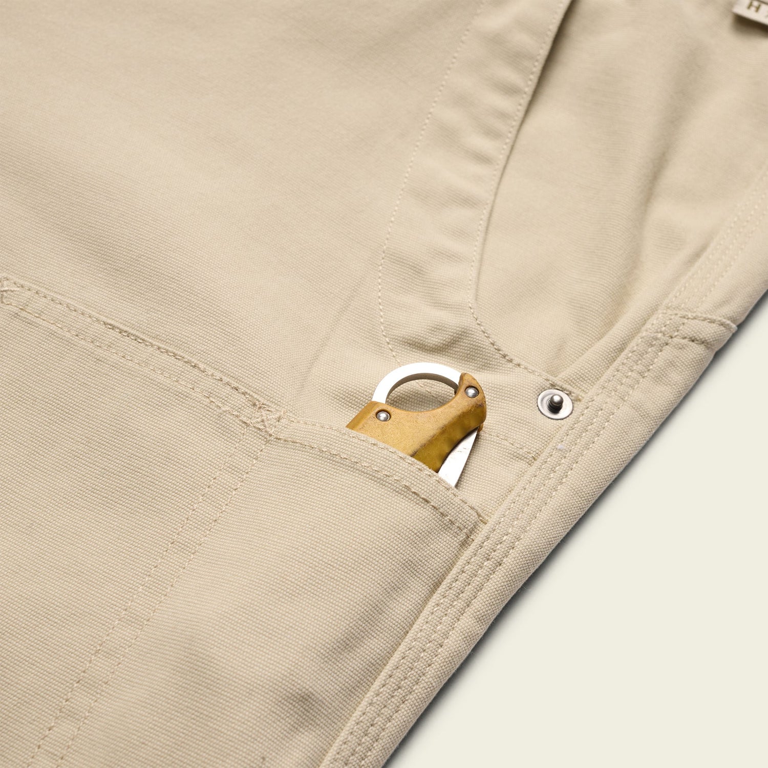 A close-up of rugged backcountry pants with a pocket knife featuring a brass handle partially visible in the front pocket. - View 5