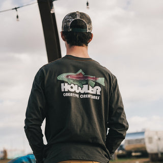 A person wearing a camouflage cap and a dark cotton-poly blend long-sleeve shirt with a colorful fish and the text “HOWLER CREATIVE CREATURES” on the back, standing outdoors under string lights for maximum comfort.