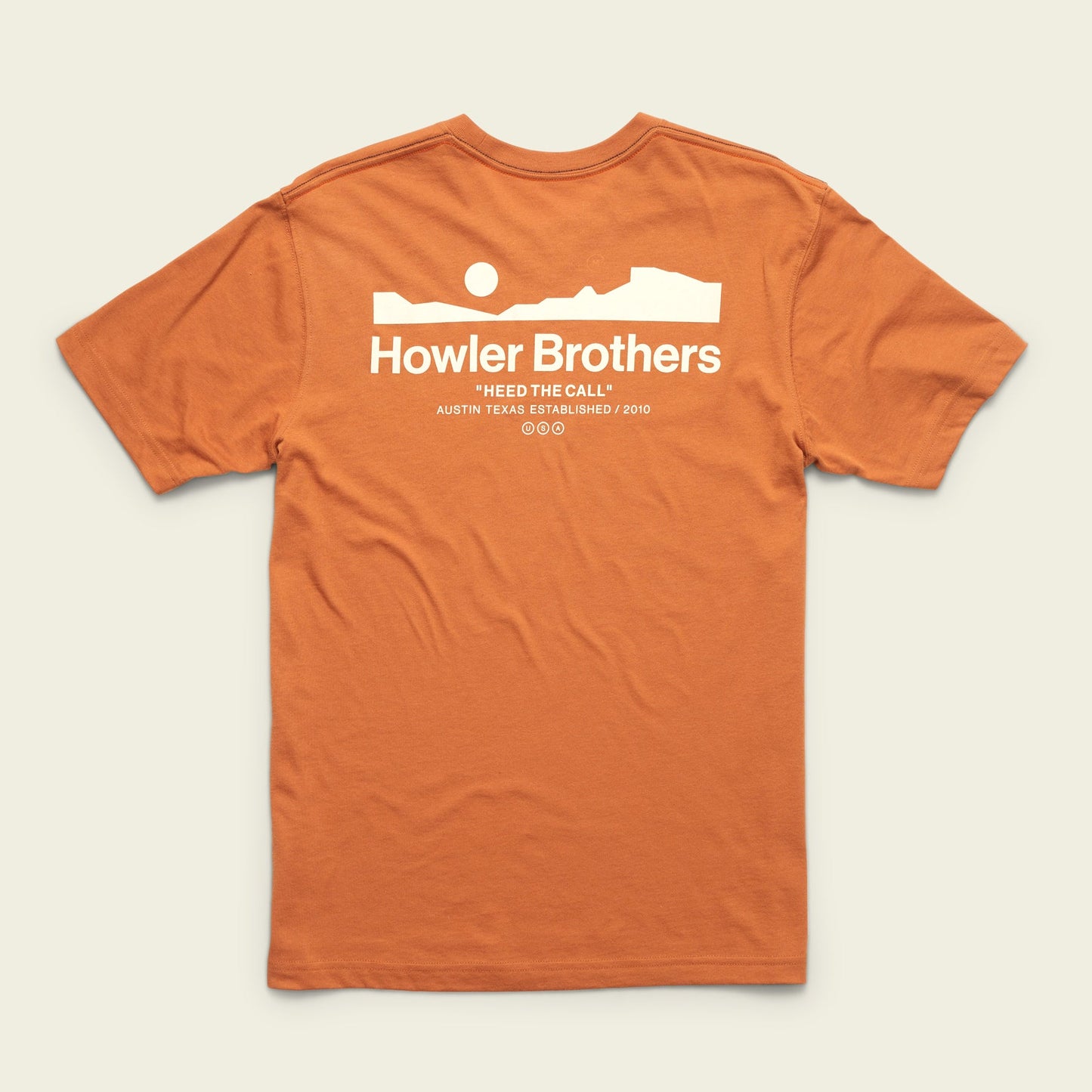 An orange cotton-poly blend t-shirt with a white graphic of a desert landscape, sun, and rock formation. The text reads Howler Brothers and Heed The Call with Austin Texas Established 2010 below for maximum comfort. - View 1