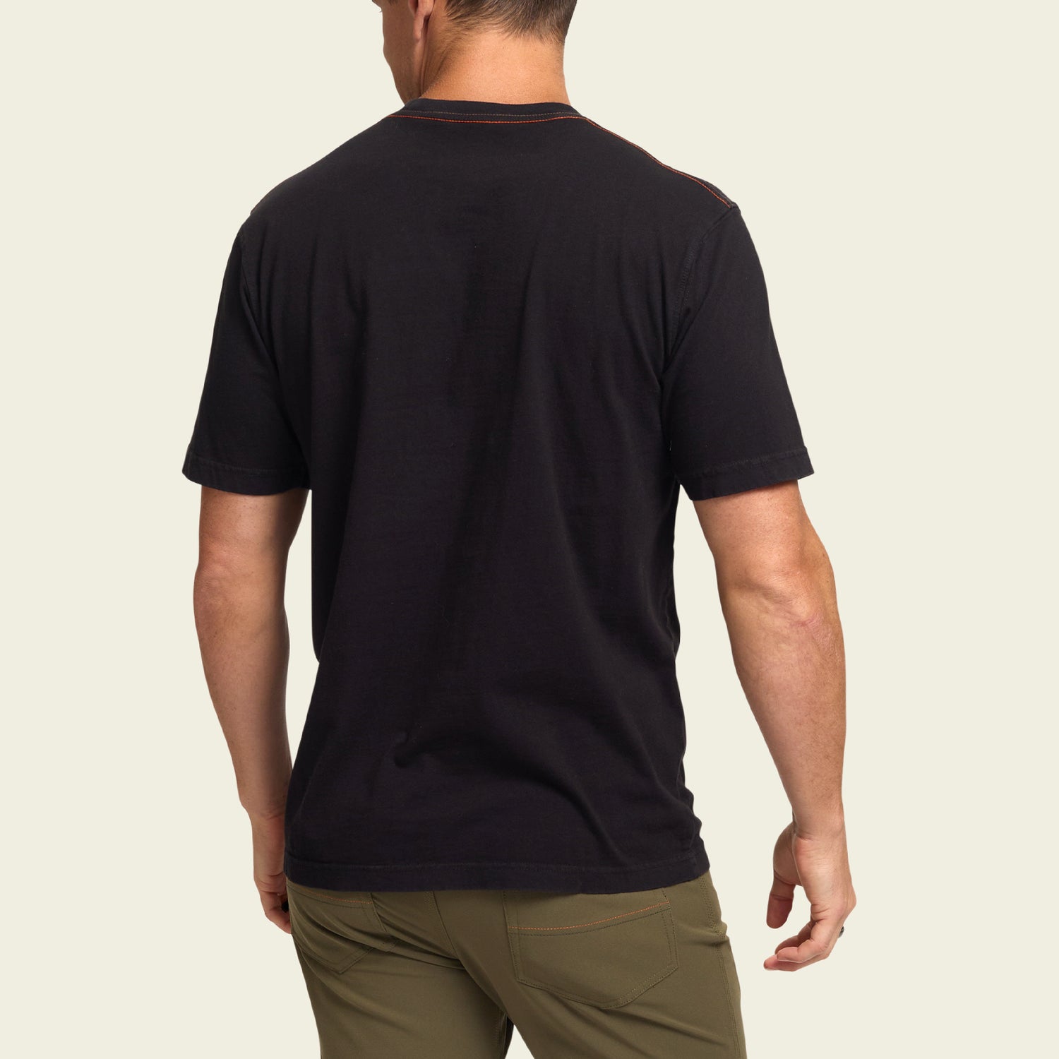 A man is standing with his back to the camera, wearing a black vintage t-shirt and olive green pants against a plain, light background. - View 3