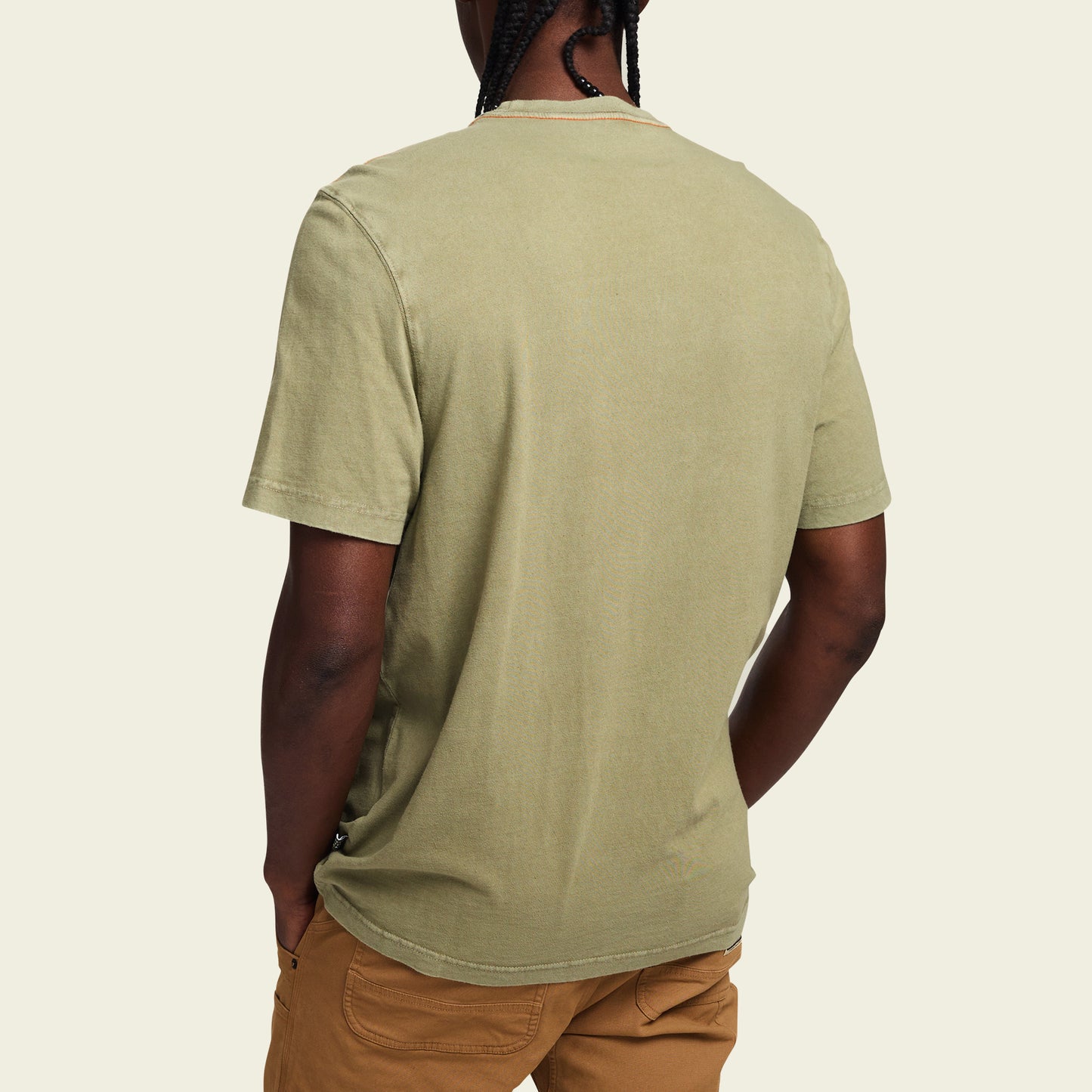 A person is shown from the back wearing a light olive green short-sleeve t-shirt reminiscent of vintage t-shirts with tan pants, standing against a plain, light background. - View 4