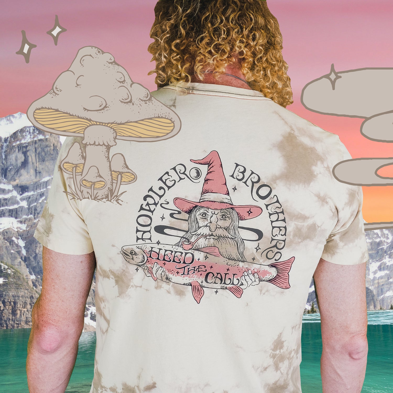 A person with curly hair faces away, wearing a tie-dye cotton t-shirt featuring a wizard holding a fish with Howler Brothers and Heed the Call text. This vintage look is accented by cartoon mushrooms, sparkles, a lake, and mountains. - View 6