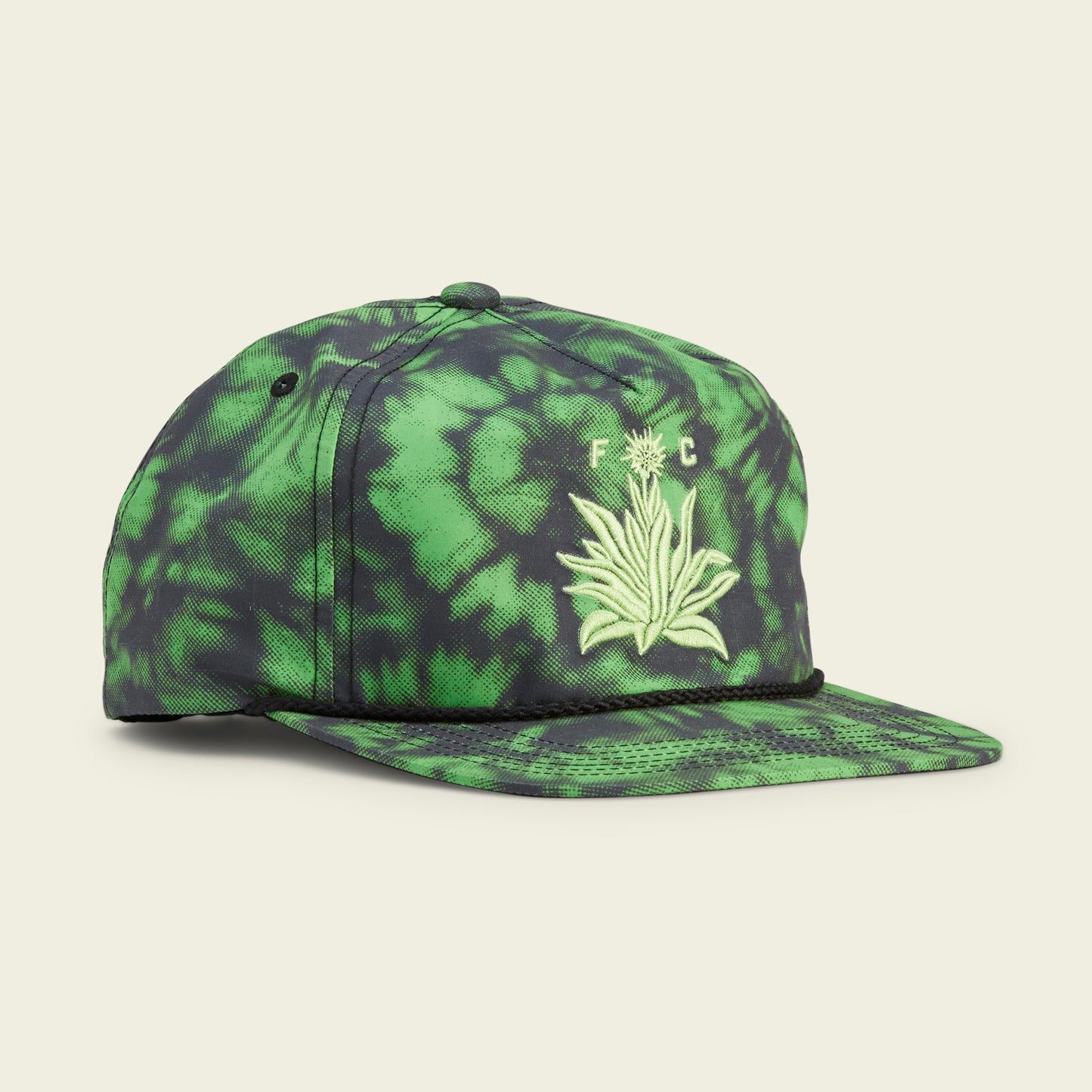 A green and black tie-dye baseball cap inspired by Austin FC, featuring an embroidered plant design and the letters F C on the front. This stylish Howler Brothers snapback has a flat brim and a decorative black rope across the crown’s base. - View 1