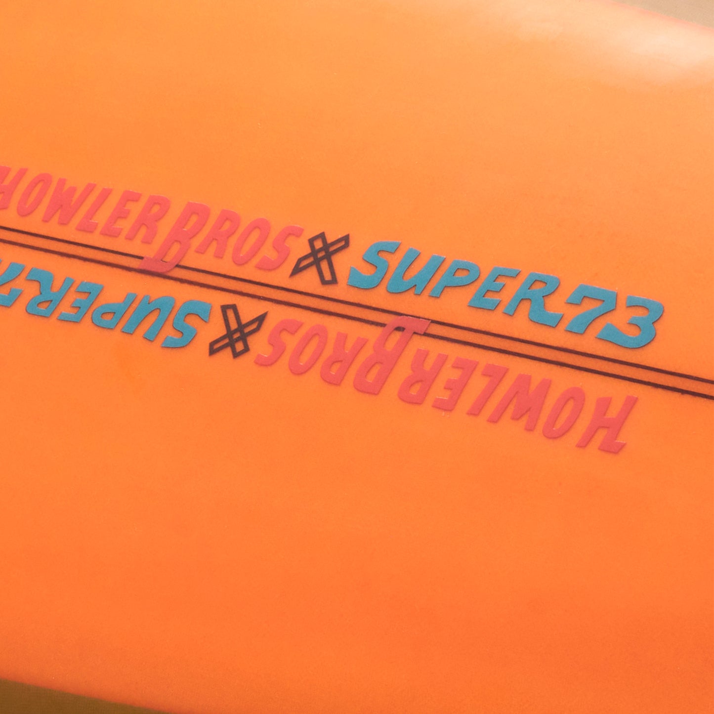 Close-up of orange surface featuring HOWLER BROS x SUPER73 repeated in pink and blue text, separated by a black line—highlighting the vibe of a Lightning Powered Surf Machine. - View 3