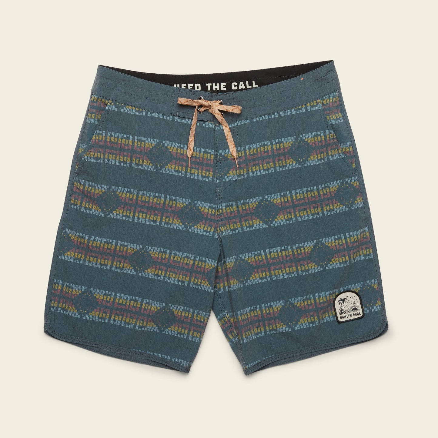 Blue patterned Bruja Boardshorts with a tan drawstring, geometric designs in muted colors, and a patch on the left leg featuring a palm tree and text—perfect stretchy boardshorts for everyday wear. - View 14